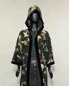 A hooded longline kimono-style jacket with a green and brown hummingbird silhouette pattern and black trim, displayed on a black mannequin against a plain light background.