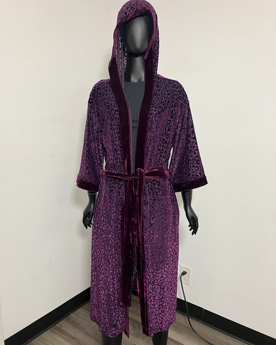 A purple leopard-print hooded robe with a matching tie belt, displayed on a black mannequin in an indoor setting against a plain wall.
