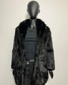 Mannequin wearing a dark fur coat and black pants on a plain background