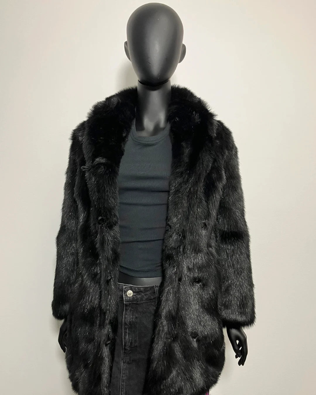 Mannequin wearing a dark fur coat and black pants on a plain background