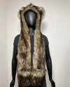 A brown and beige faux fur hood with animal ears, displayed on a black mannequin torso against a plain light gray wall.