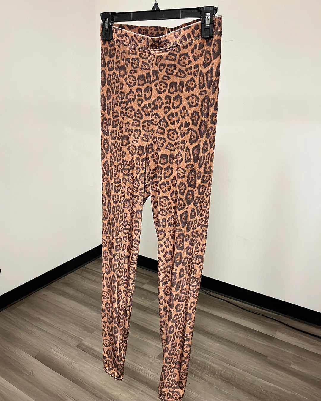 Tan and brown leopard print velvet leggings on a black hanger in front of a plain white wall.