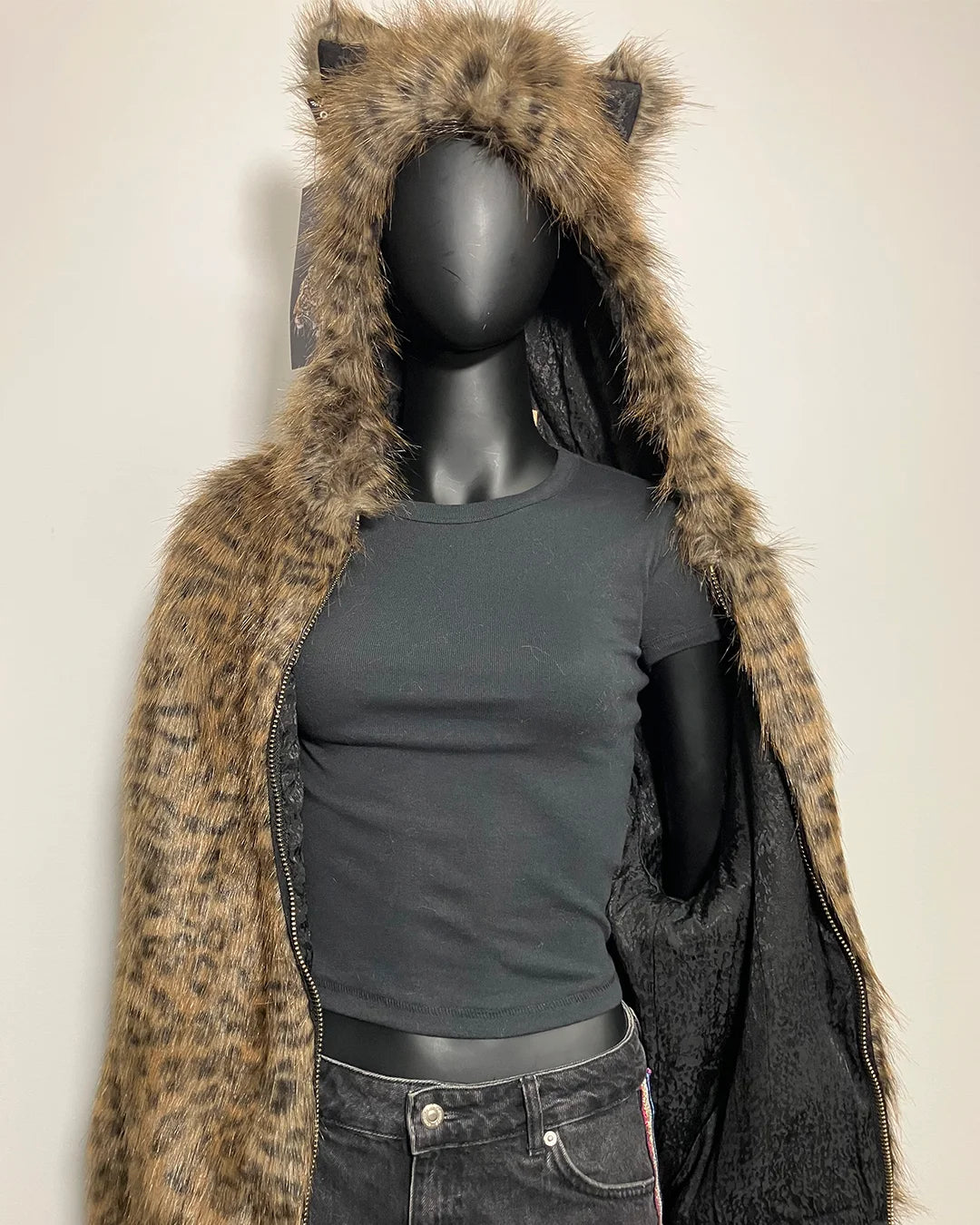 Mannequin wearing a black t-shirt and fur-lined coat with animal ears on a plain background