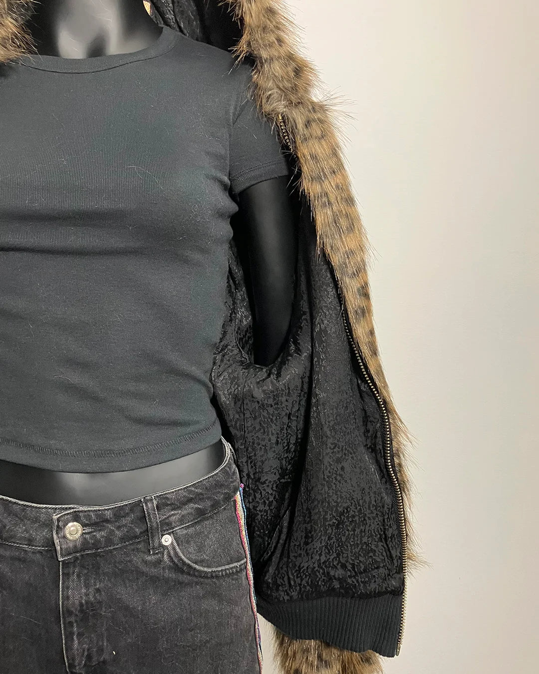 Mannequin wearing a black jacket with fur trim on a plain background