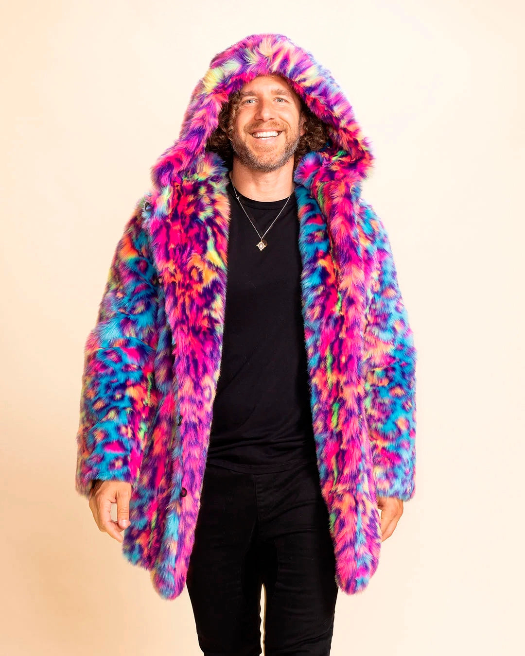 A Man wearing a colorful pink & blue faux fur leopard print coat with a large oversized hood on, smiling walking towards the camera, against a beige background. SpiritHoods Made to Order Neon Disco Cat Faux Fur Coat for Men