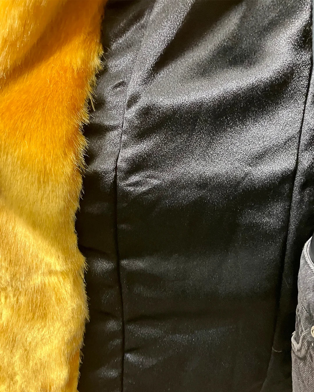 Close-up of a black satin lining in the Golden Wolf Faux Fur jacket with yellow fur trim