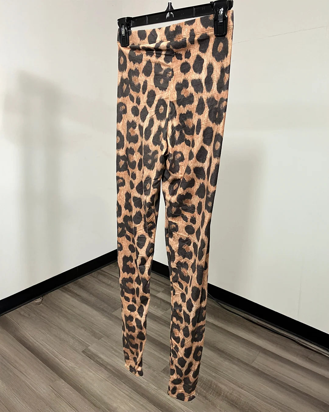 Back view of leopard print leggings hanging on a black hanger against a white wall and wood-look floor.