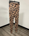 Leopard print leggings hanging on a black hanger against a white wall and wood-look floor.
