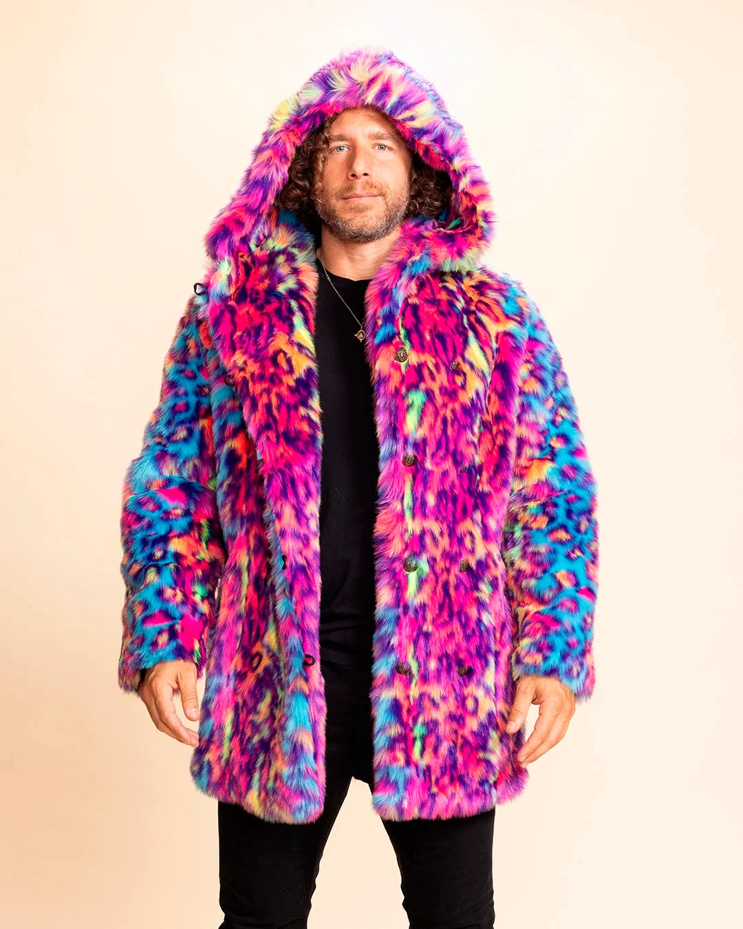 A Man wearing a colorful fur-free fur coat against a beige background. Neon Pinks, Neon Blue, Neon Yellow leopard print throughout, that glows under UV Blacklight. Featuring SpiritHoods oversized Hood and leopard face pea-coat buttons.  Custom Made Coats and Made to Order Faux Fur Jackets