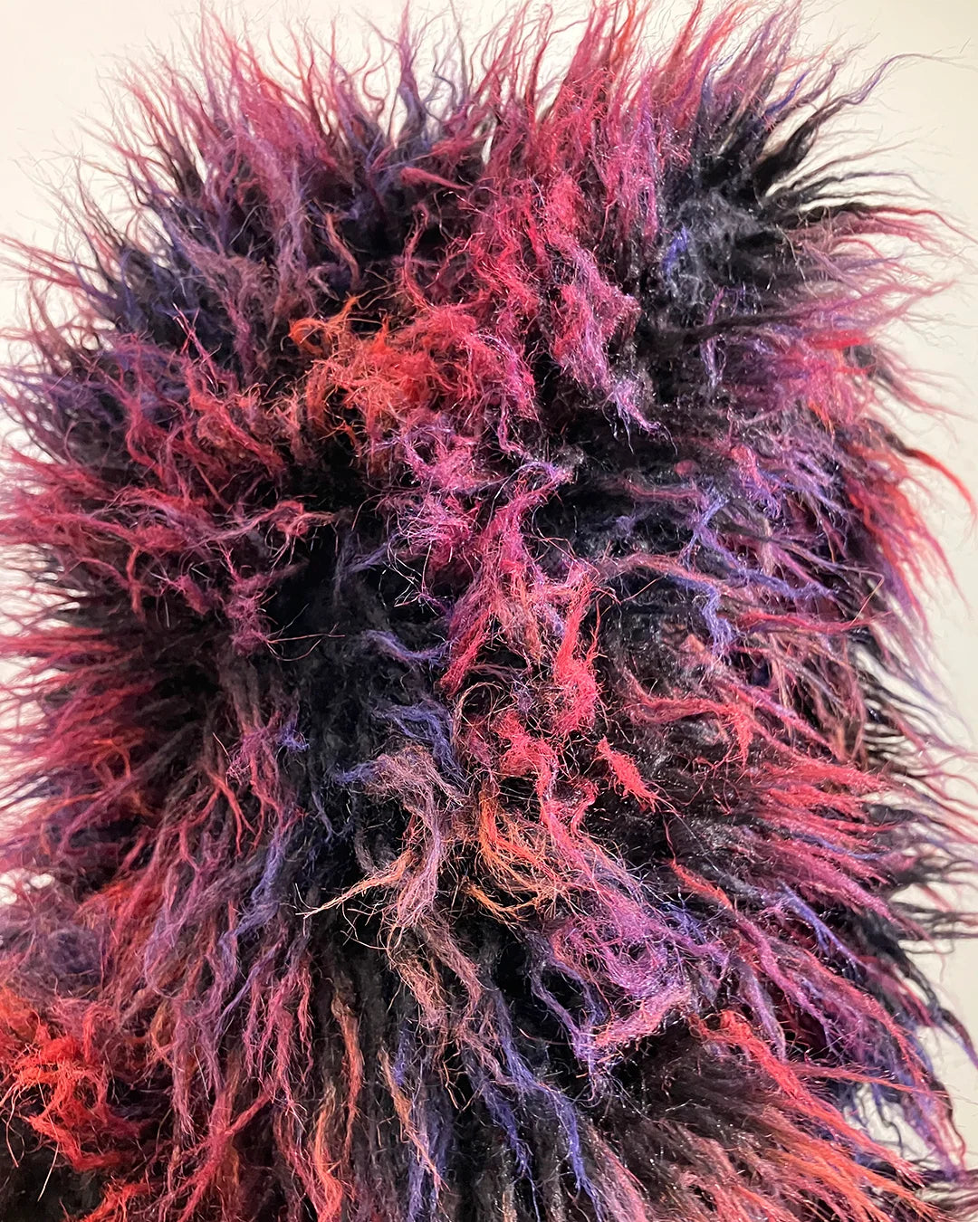 Close-up of a multicolored plush fake fur vest's oversized hood with pink, purple, and red hues.
