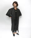 A man modeling a long, open-front black textured kimono-style robe over a black outfit, standing against a plain white studio background.