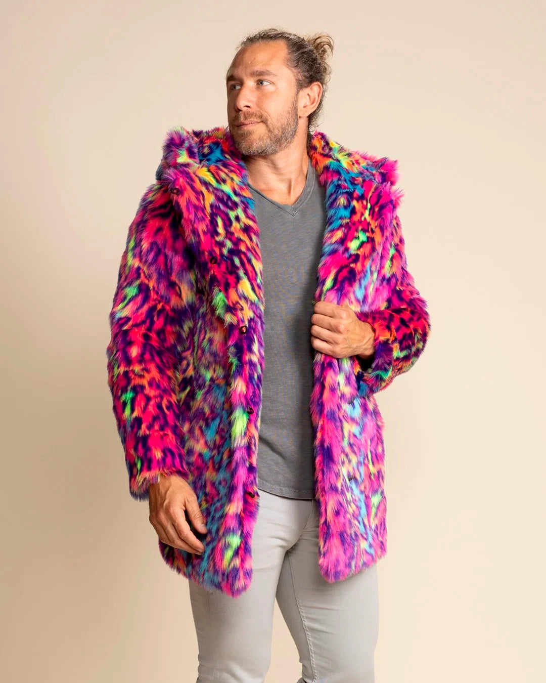 A Man wearing a colorful pink & blue faux fur leopard print coat with a large oversized hood on, smiling walking towards the camera, against a beige background. SpiritHoods Made to Order Neon Disco Cat Faux Fur Coat for Men