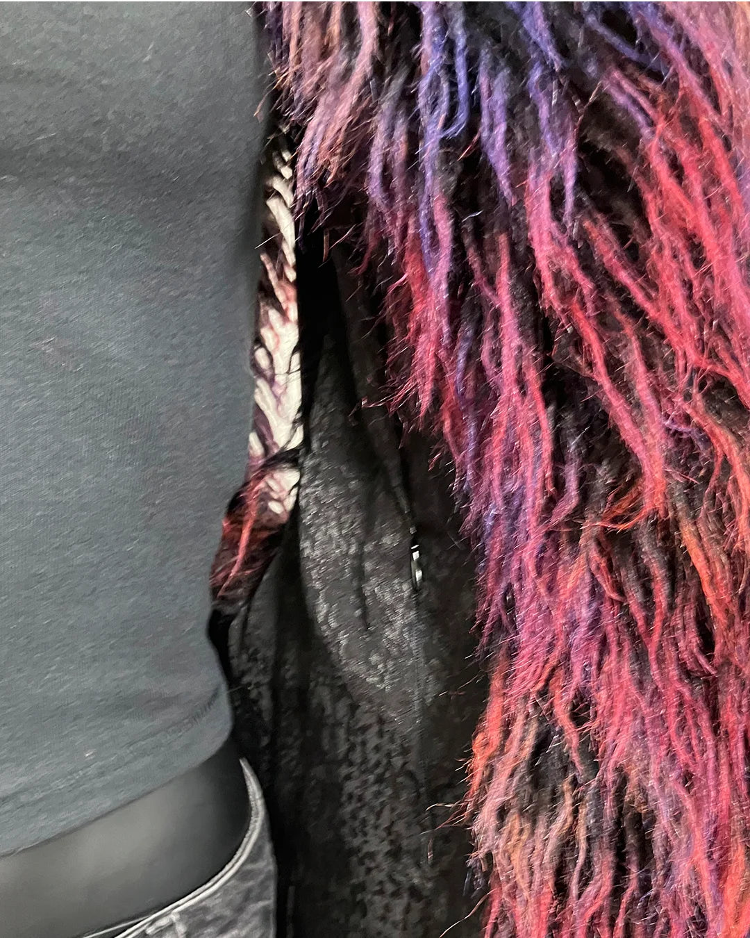 Close-up of a person wearing a gray shirt with a colorful, textured fake fur vest draped over them. Showing the inner zipper pocket