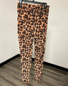 Leopard print leggings with a front flap-pocket hanging on a black hanger against a white wall and wood-look floor.