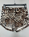 Leopard print shorts in a plush velvet-like fabric, hanging from a black plastic hanger against a light gray wall.