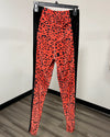 Bright orange and black leopard print leggings hanging from a black hanger against a white wall and wood-look floor.