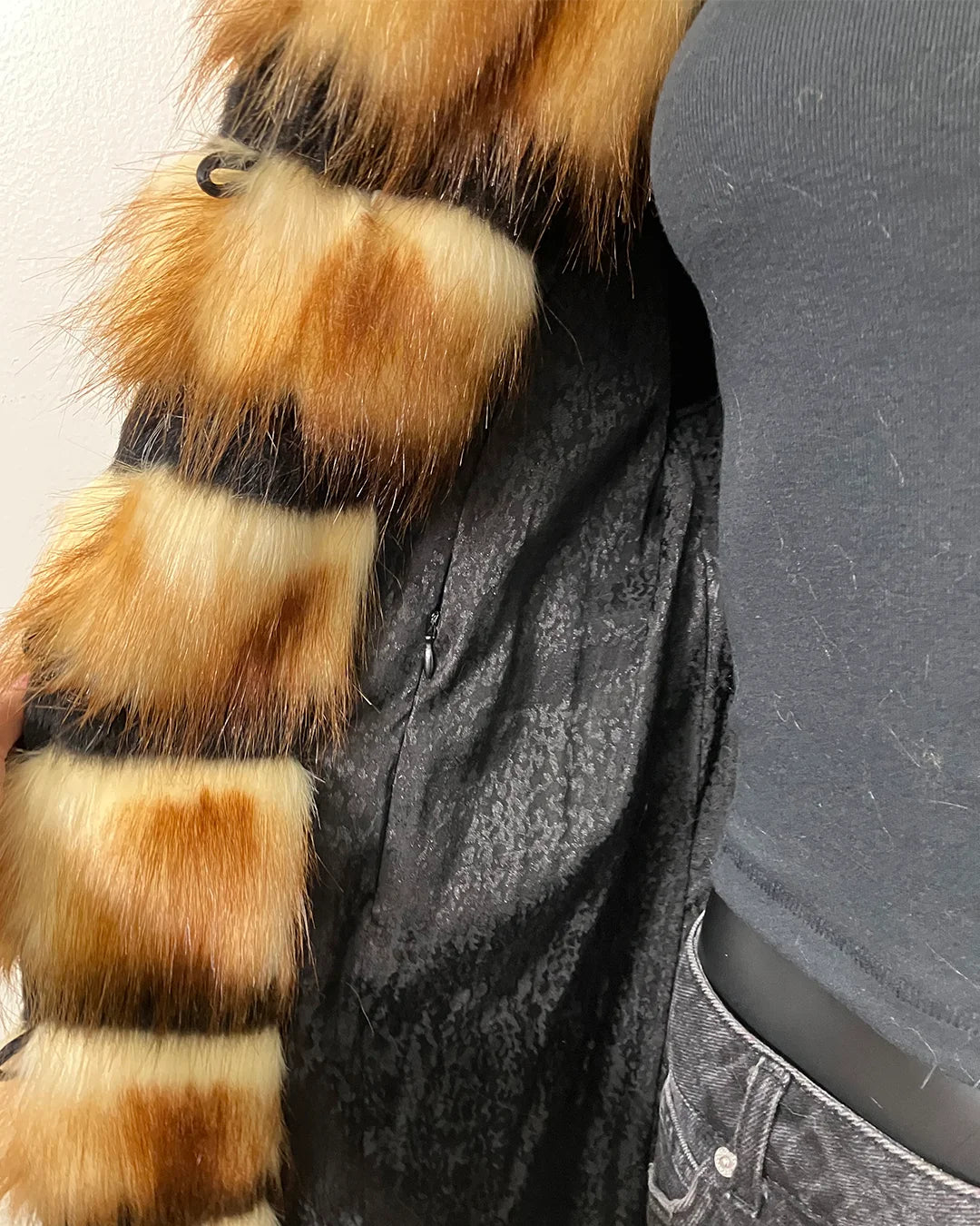 Close-up of a faux fur coats inner liner showing the black fabric with a light snakeskin print, and inner zipper pocket.