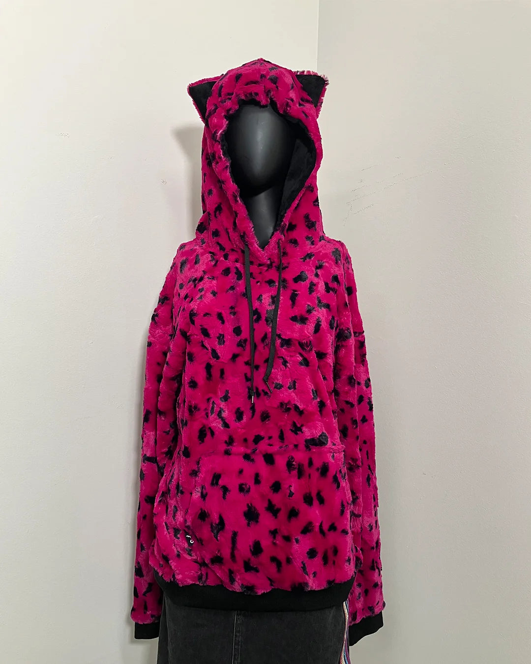 black mannequin wearing spirithoods hot pink cheetah faux fur hoodie with a hood and small ears against white wall