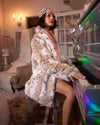 A Woman wearing SpiritHoods Best Selling Siberian Snow Leopard Faux Fur Coat while playing the piano in a whimsical room.