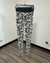 Zebra-print leggings hanging on a black hanger against a white wall with wood-look flooring.