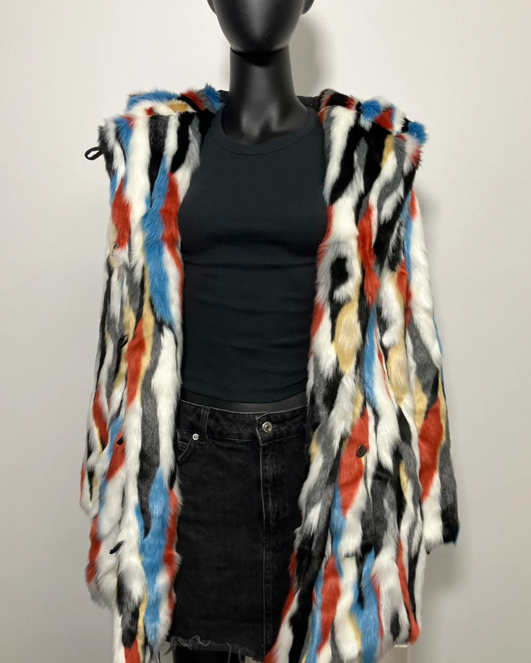 Mannequin wearing a colorful faux fur coat over a black shirt and jeans on a plain background