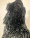 Close-up of a textured, black-colored fake fur with a wolf face button on a beige background. SpiritHoods XXS Sizing Black Wolf Online Sample Sale Style.