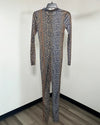 A long-sleeve full-body one-piece jumpsuit with an abstract leopard-like pattern in muted brown, gray, and black, hanging on a black hanger against a plain off-white wall.