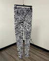 Black and white leopard print leggings hanging on a black hanger against an off-white wall with a wood floor.