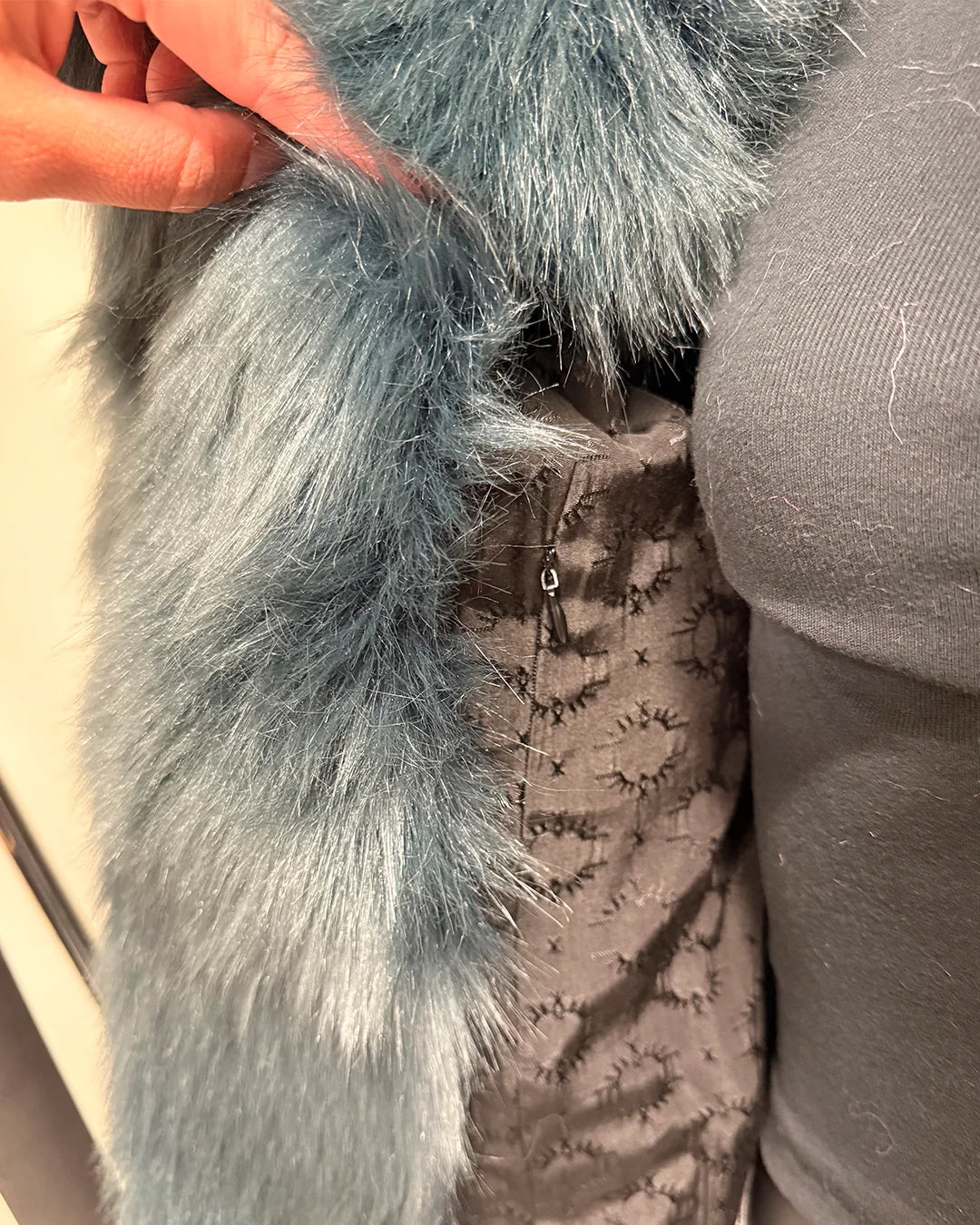 Close-up of a gray/blue fake fur-lined coat with a textured pattern. showing the inner lining with SpiritHoods logo and inner zipper pocket