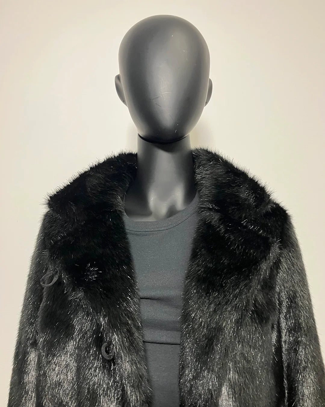 Mannequin wearing a black fake fur coat with a plain background
