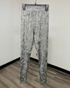 Greenish gray and black snakeskin print leggings hanging on a black hanger against a plain white wall with a wood floor.