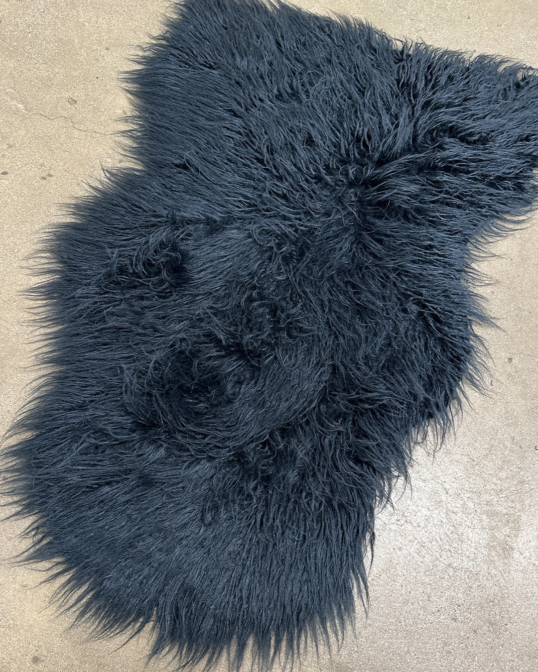 Dark blue fluffy faux fur rug on a concrete floor