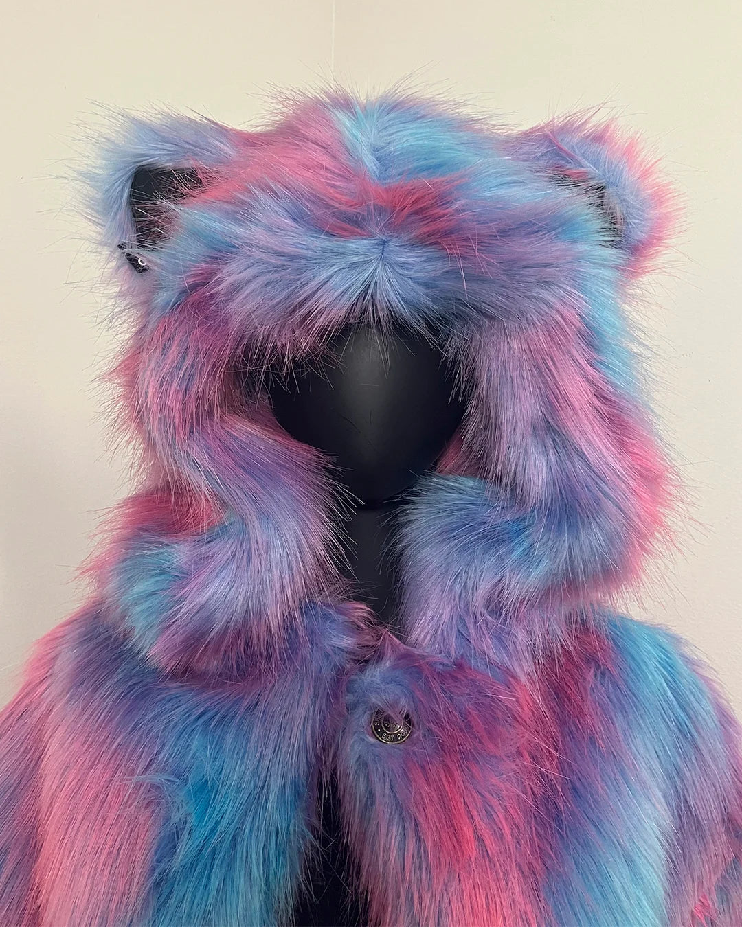 Mannequin wearing a colorful fake fur coat with pink and blue hues on a plain background