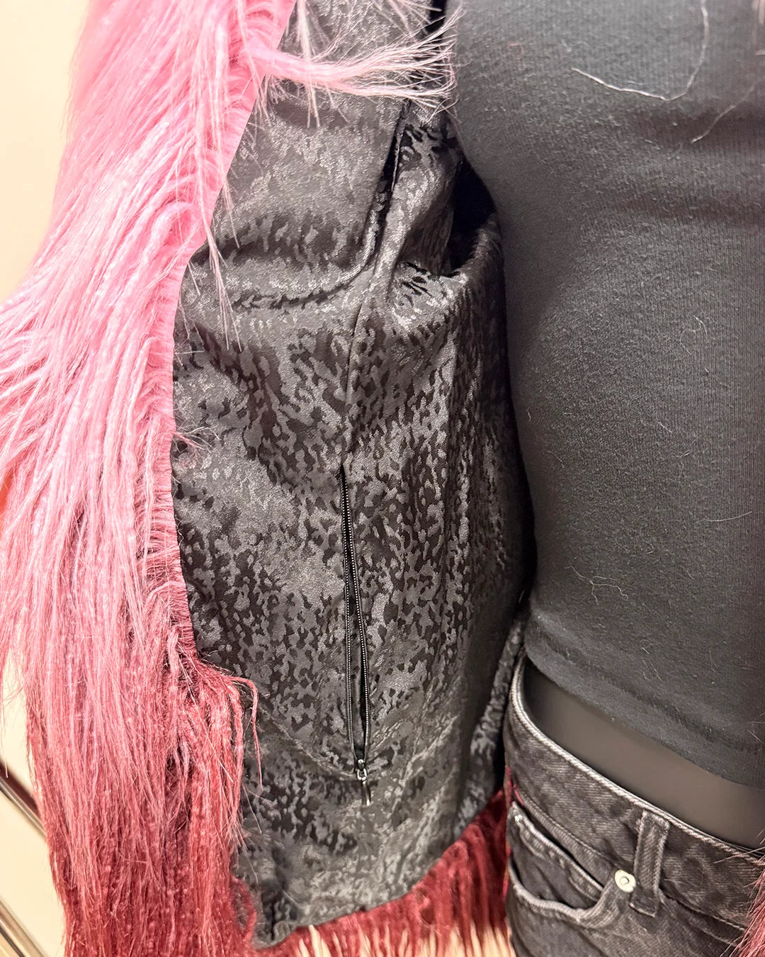 Close-up of a mannequin wearing a two-tone pink/maroon faux fur bomber jacket with a black faux snakeskin liner and inner zipper pocket