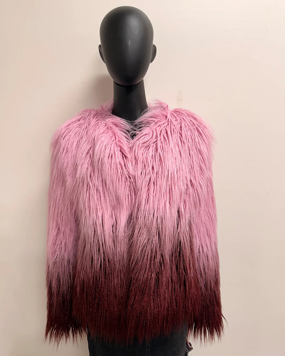Mannequin wearing a pink and maroon ombre gradient faux fur coat against a beige background