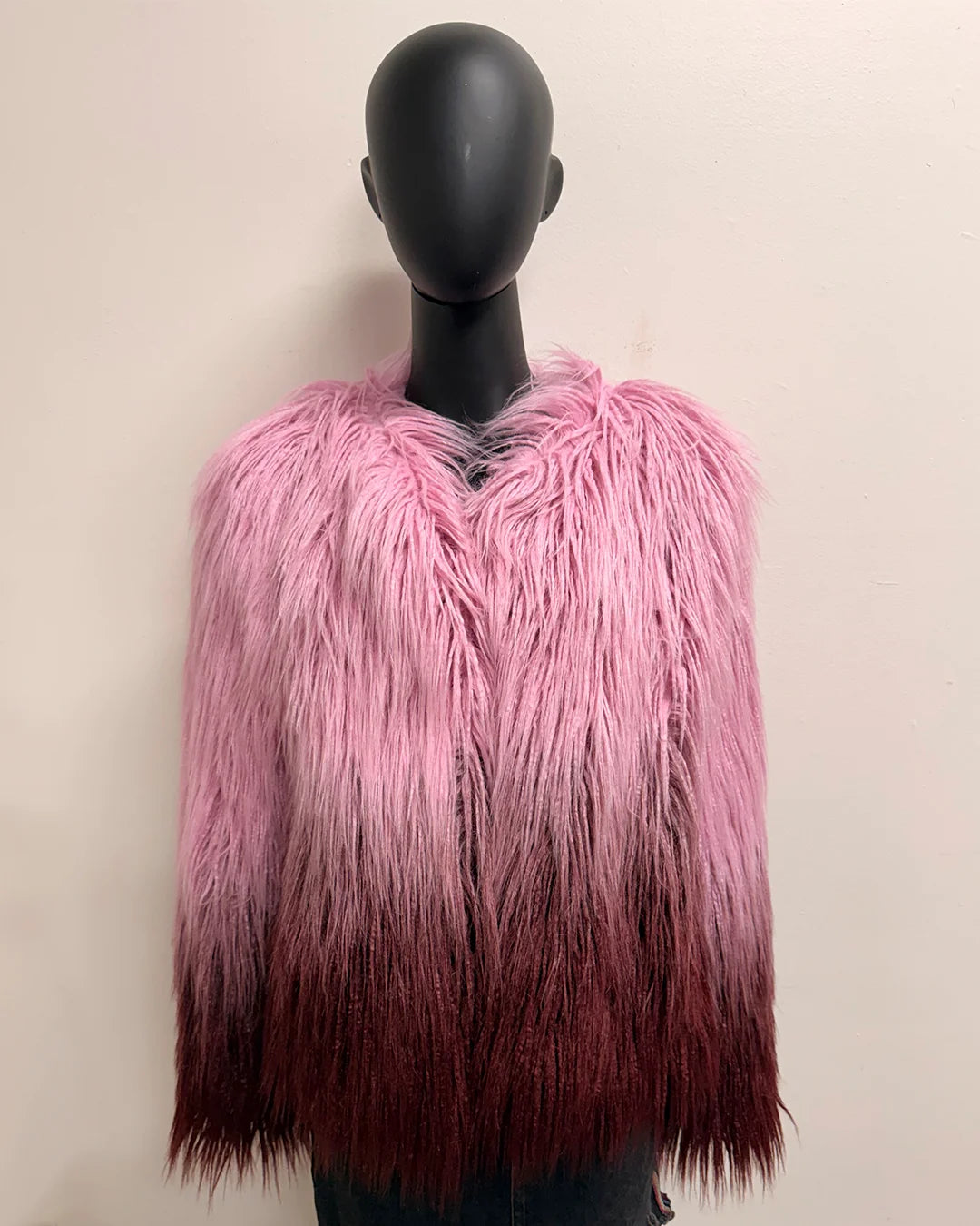 Mannequin wearing a pink and maroon ombre faux fur vest against a beige background