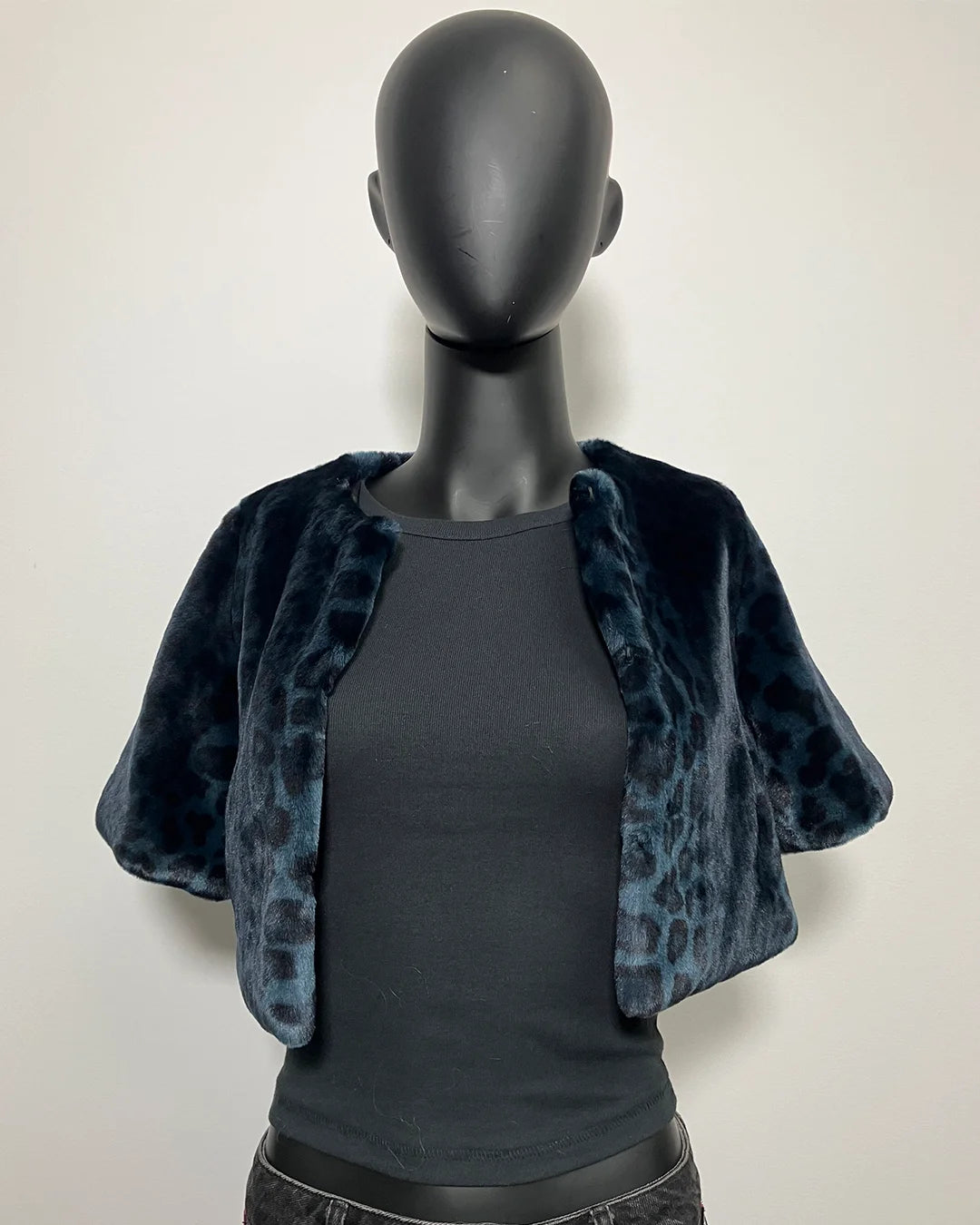 Mannequin wearing a blue leopard print shrug over a black top against a white background