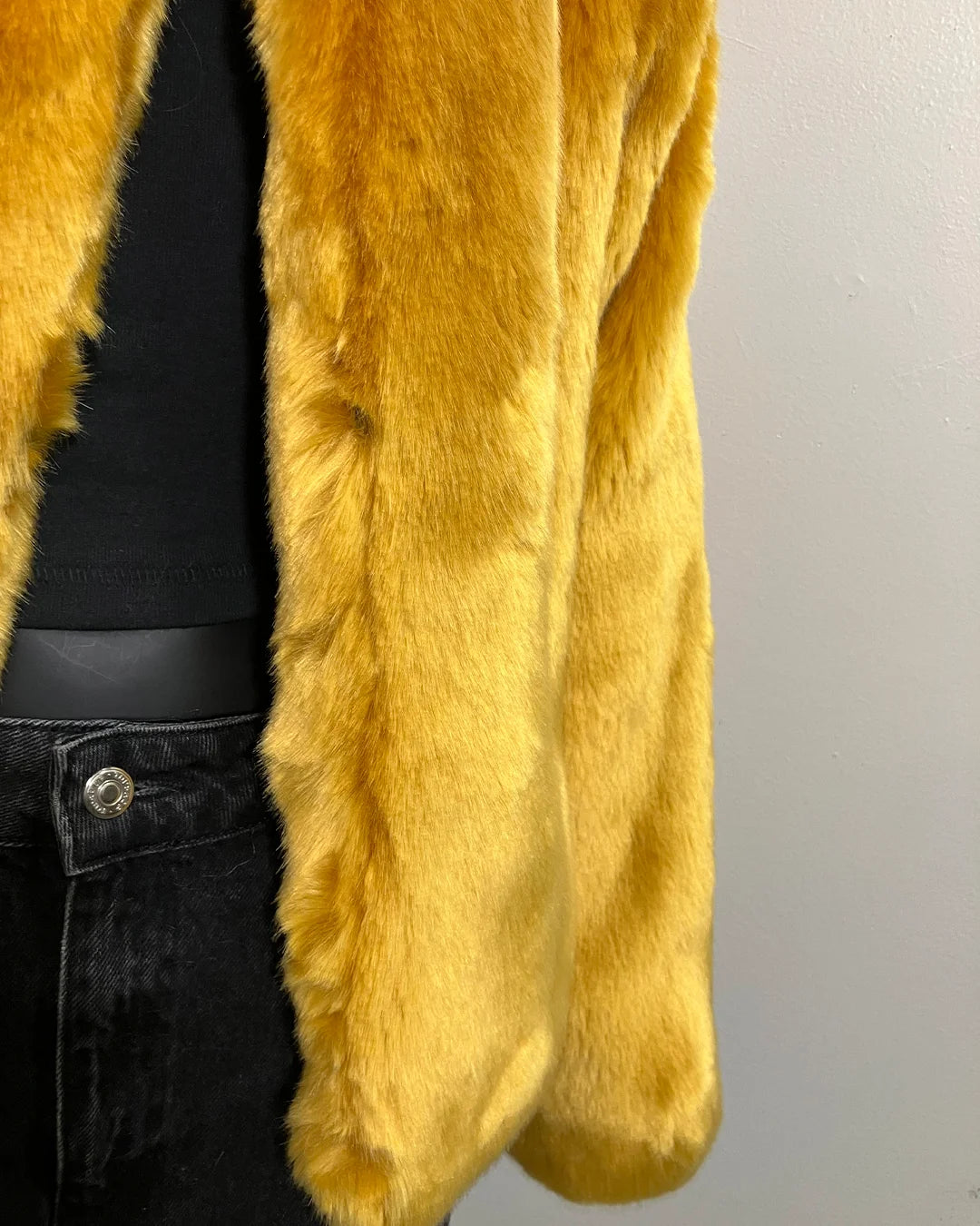 Close-up of a golden bright yellow plush faux fur bomber jacket coat with a plain background