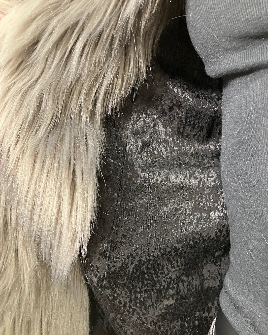 Close-up of a textured black snakeskin fabric with a grey faux fur trim on a dark background