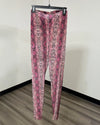 Pink and red snakeskin print leggings hanging on a black hanger against a plain off-white wall.