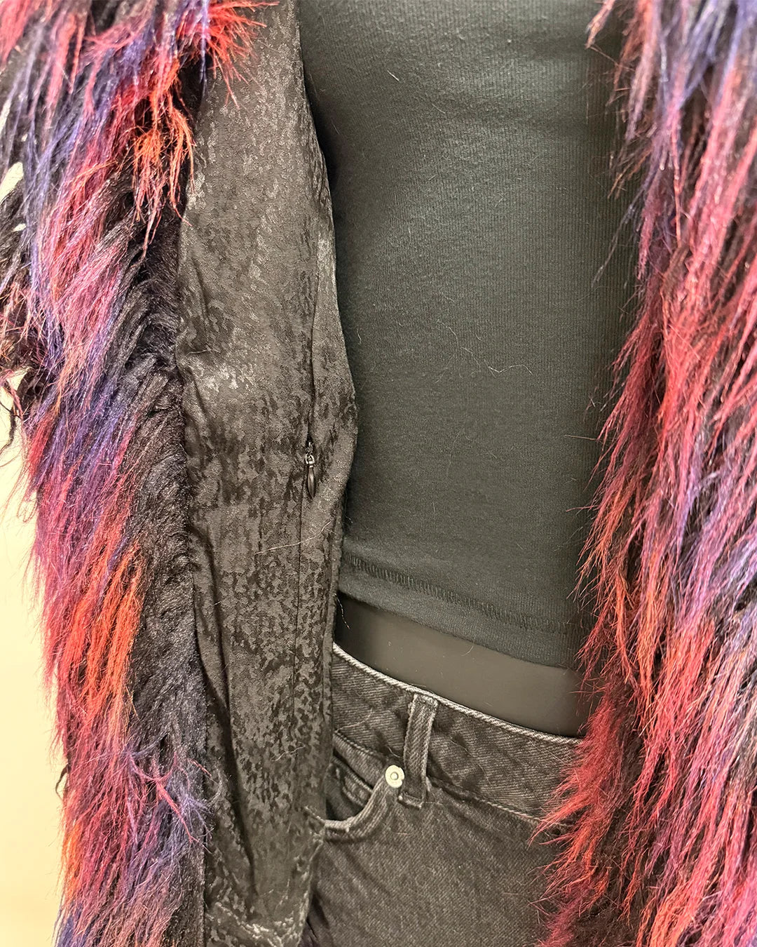 Person wearing a dark gray distressed alpaca inspired faux fur jacket with colorful fur trim on a plain background