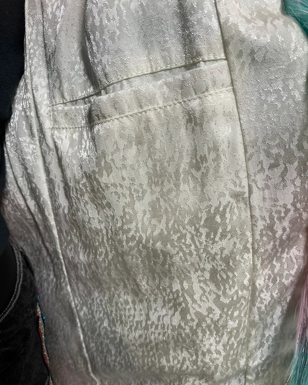 Close-up of a textured lining in the spirithoods Doll Party Faux Fur Calf Length Coat showing the inner welt pocket with a subtle snakeskin pattern
