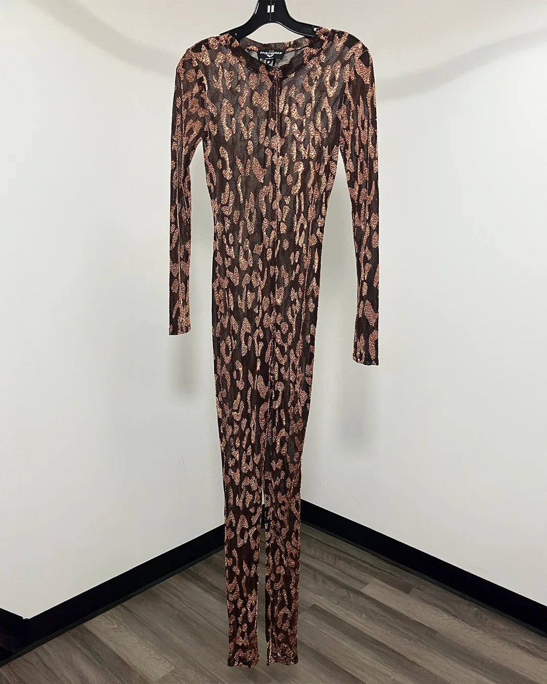 A long-sleeve, full-length leopard print jumpsuit hanging on a black hanger against a plain white wall with a wood-look floor.
