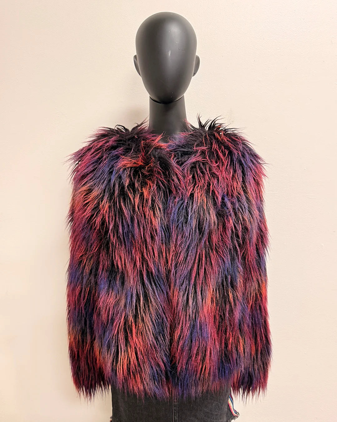 Mannequin wearing a colorful fake fur bomber jacket against a plain background