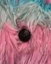 Close-up of a fluffy pink, green, and black object with a central button.