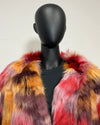 A multicolor faux fur jacket with red, orange, yellow, and purple tones, displayed on a black mannequin torso against a plain off-white wall.