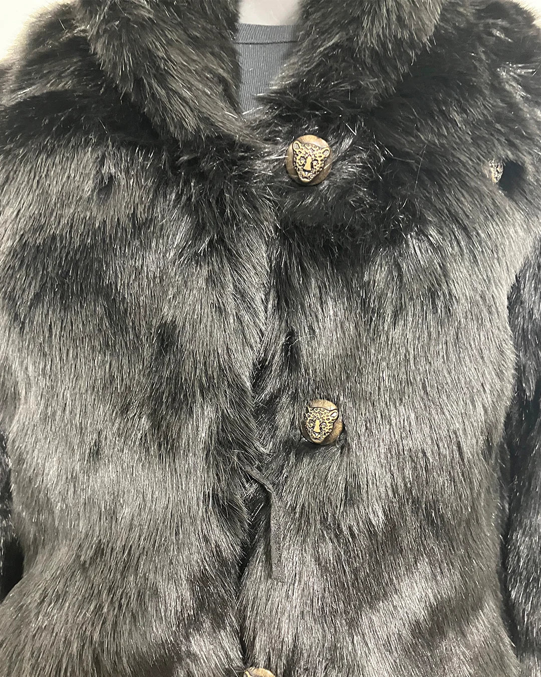 Close-up photo of the black fake fur coat with decorative leopard face buttons. Also showing the 2nd row button loop is broken. 