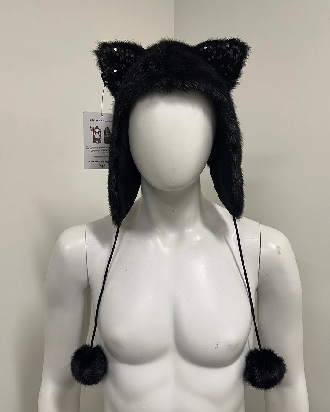 Black furry hat with cat ears and pom-poms on a mannequin 