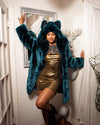 A Woman wearing a plush blue faux fur coat with an oversized hood and wolf ears in a whimsical room with mirrors and a faux deer head.