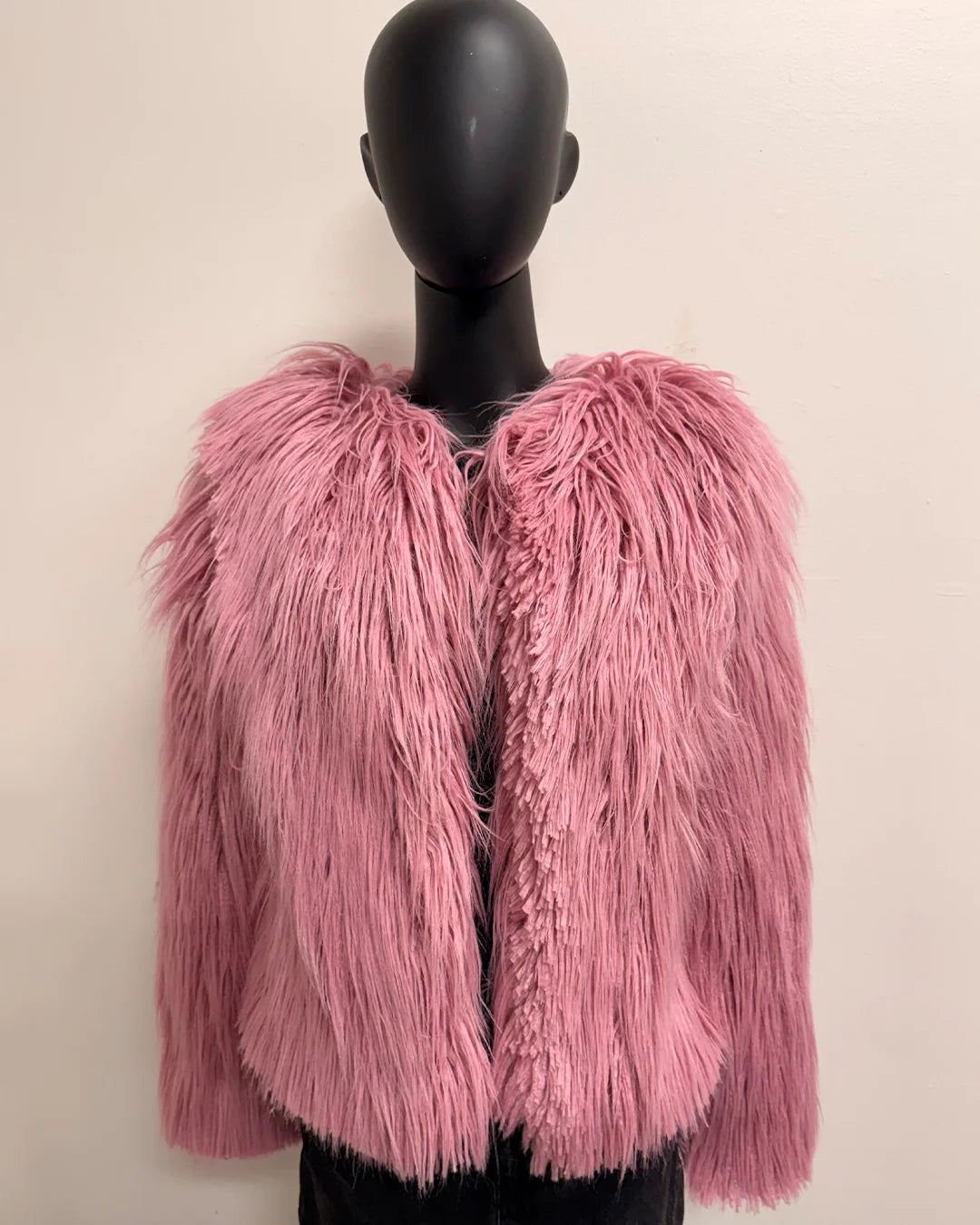 Pink fluffy jacket on a mannequin against a plain background